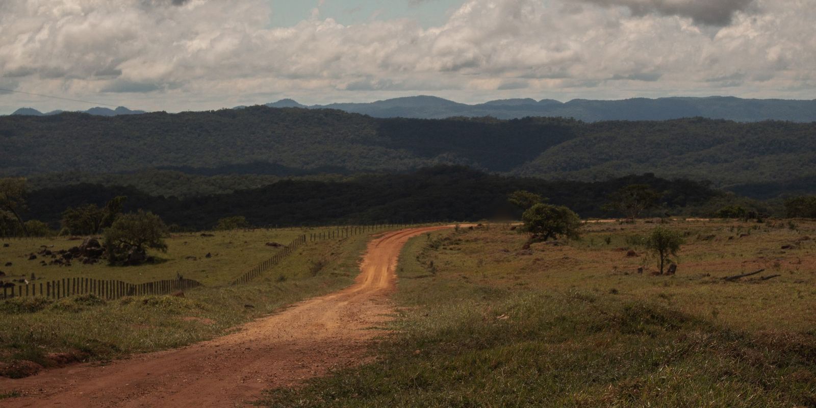 Estrada de terra vermelha entre pastos e cerrado na região de Bonito, em Mato Grosso do Sul, com serras ao fundo